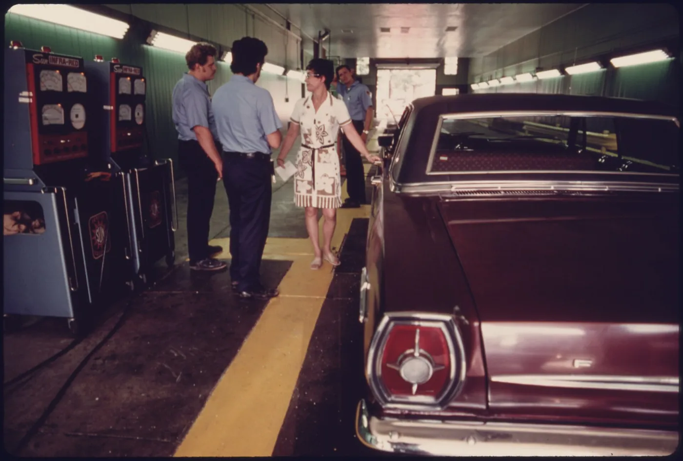 A driver talks with inspectors after her car failed an emission inspection, 1975
